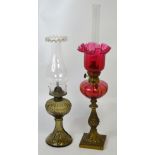 A brass oil lamp with cranberry glass font and shade,