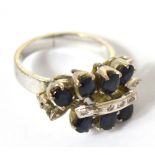 An 18ct white gold dress ring set with sapphires and tiny diamonds in a scrolling floral design,