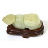 A Chinese pale green jade carved chi chi with russet inclusion to the back and on shaped wooden