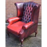 A red Chesterfield style button back armchair on cabriole legs.