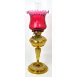 A Victorian brass oil lamp with fluted column style support and cranberry shade, height 63cm.