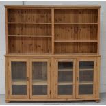A large pine bookcase, three shelves with boarded back above earlier glazed bottom section,