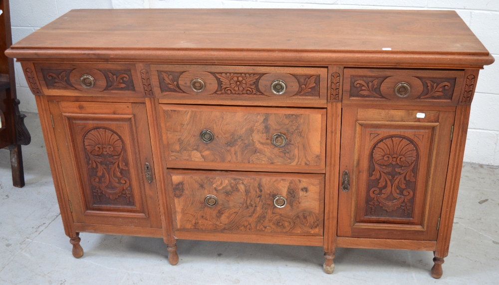 A 20th century walnut sideboard with three central drawers and two heavily carved cupboard doors to