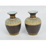 A pair of Doulton Lambeth Silicon relief moulded gilt heightened small vases on a brown ground,