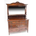 An Edwardian Arts and Crafts walnut sideboard with mirrored back and shaped pediment raised on two