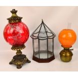 A decorative table lamp modelled as an oil lamp with large globular cranberry glass reservoir above