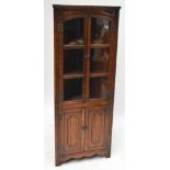 A reproduction oak freestanding corner cupboard with glazed upper section and linenfold decorated