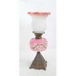 A Victorian cast iron oil lamp with pink glass floral hand painted reservoir and opaque white and