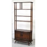 An Ercol elm shelving/display unit with lower two-door cupboard section on rounded tapering