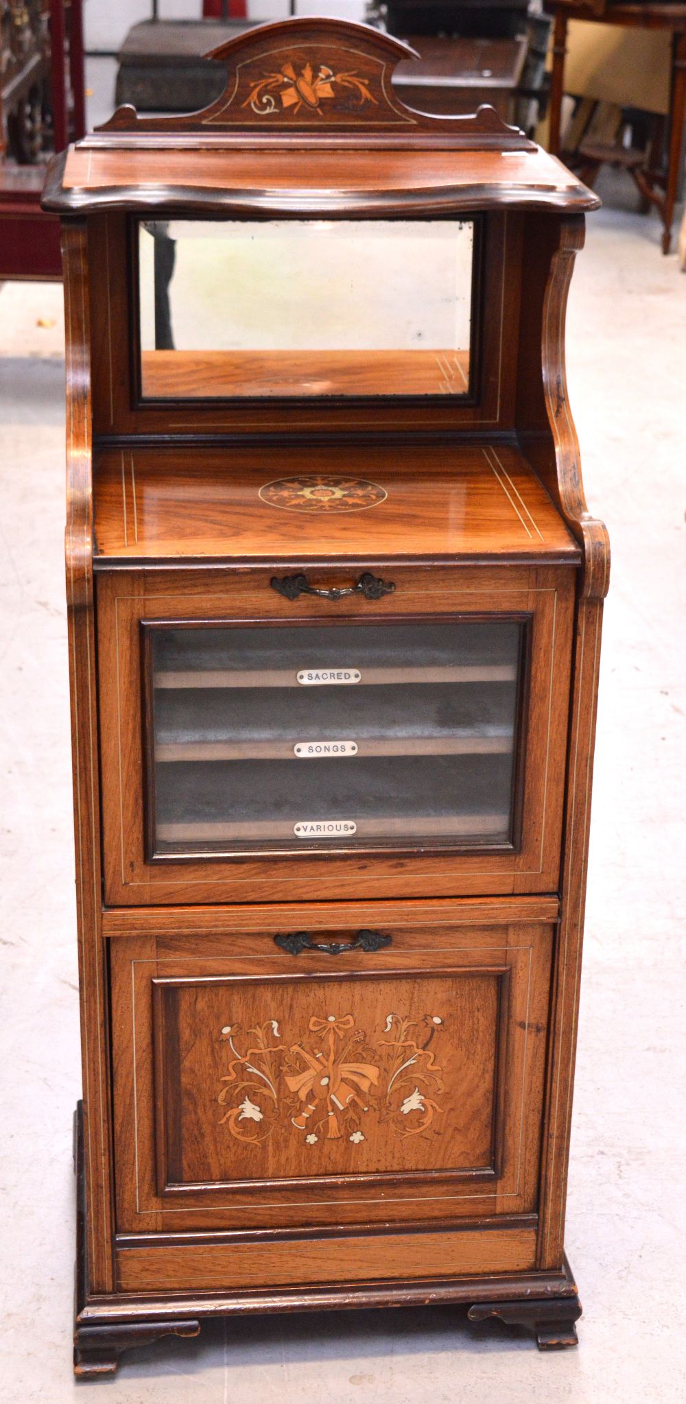 An Edwardian inlaid walnut music cabinet with bevel edge mirror back above fall-front glazed door