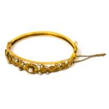 A yellow metal bangle with floral and foliate design to the top, set with small seed pearls,