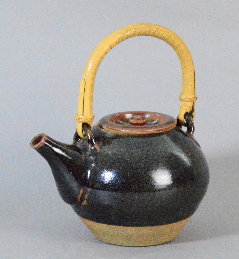 Leach Pottery; a stoneware teapot with cane handle covered in tenmoku breaking to kaki glaze,