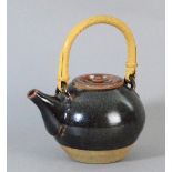 Leach Pottery; a stoneware teapot with cane handle covered in tenmoku breaking to kaki glaze,