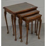 A nest of three walnut side tables with glass tops on cabriole legs and paw feet.