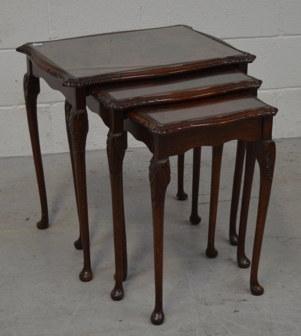 A nest of three reproduction mahogany tables with glass tops on cabriole legs and paw feet.