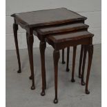 A nest of three reproduction mahogany tables with glass tops on cabriole legs and paw feet.