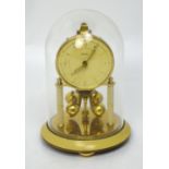 A brass anniversary clock in a glass dome, dial set with batons and Arabic numerals, height 17cm.