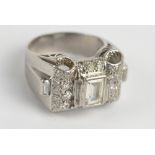 A white metal diamond cluster ring, the central emerald cut diamond weighing approx. 0.