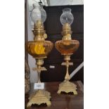 A PAIR OF EARLY 20TH CENTURY OIL LAMPS WITH AMBER GLASS RESERVOIRS.