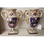 A Pair of Derby Twin Handles Urns; with gilt floral decoration raised on square pedestal bases, some