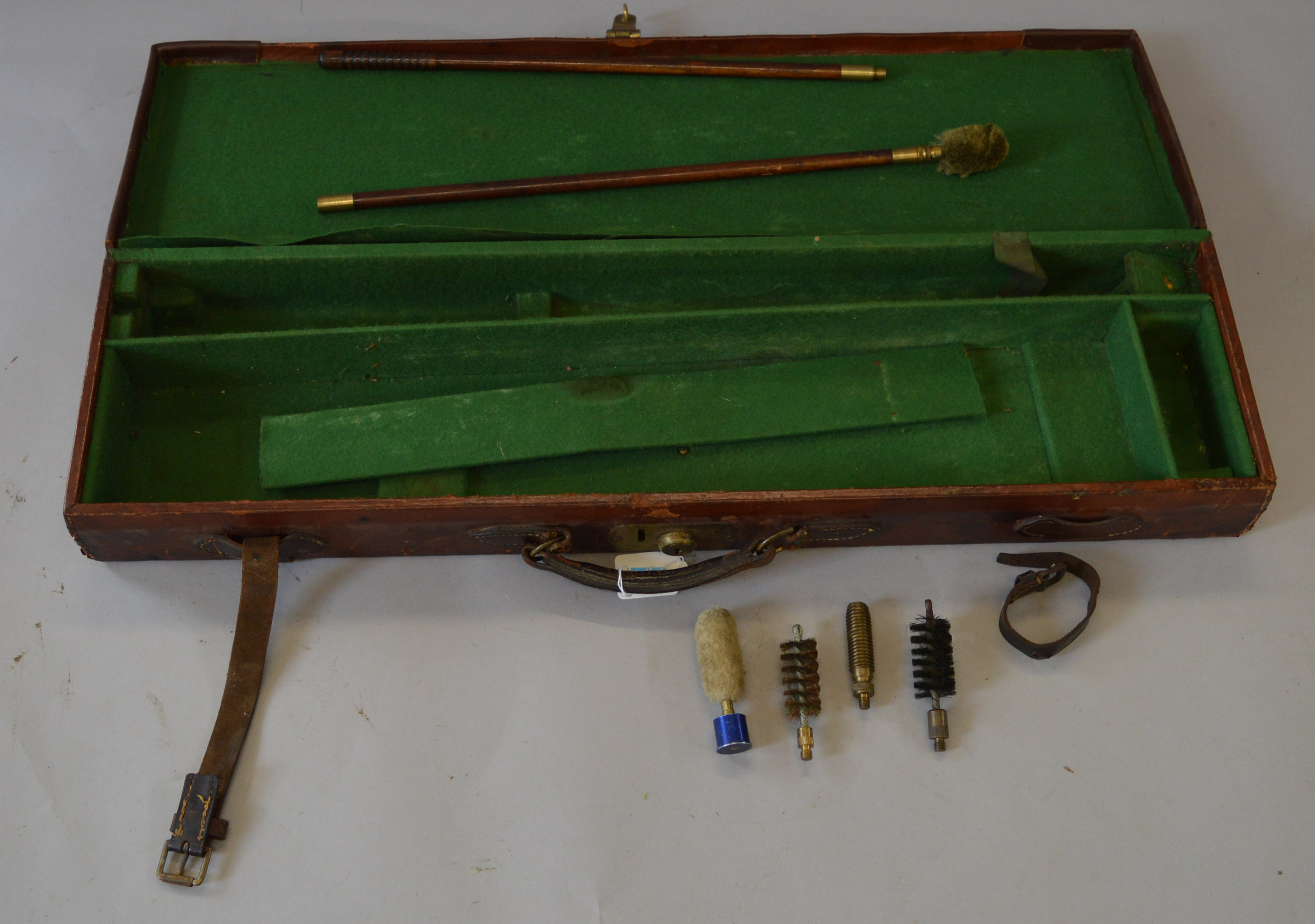 A hard leather gun case lined with green baize. Includes vintage cleaning brushes and accessories.