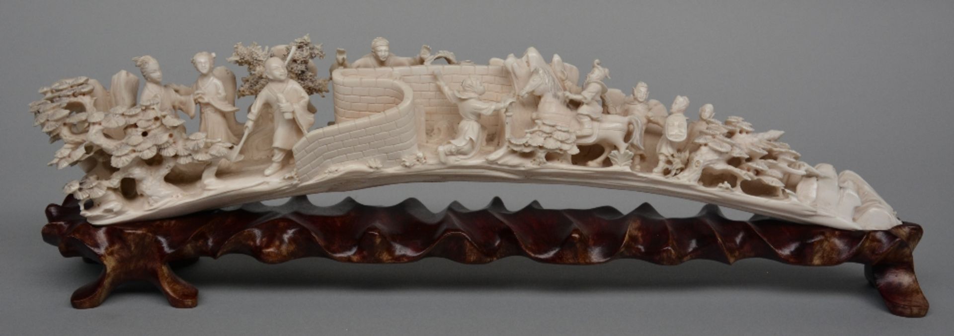 An ivory tusk carved with animated scenes, on a matching wooden base, first half of 20thC, L 45,5