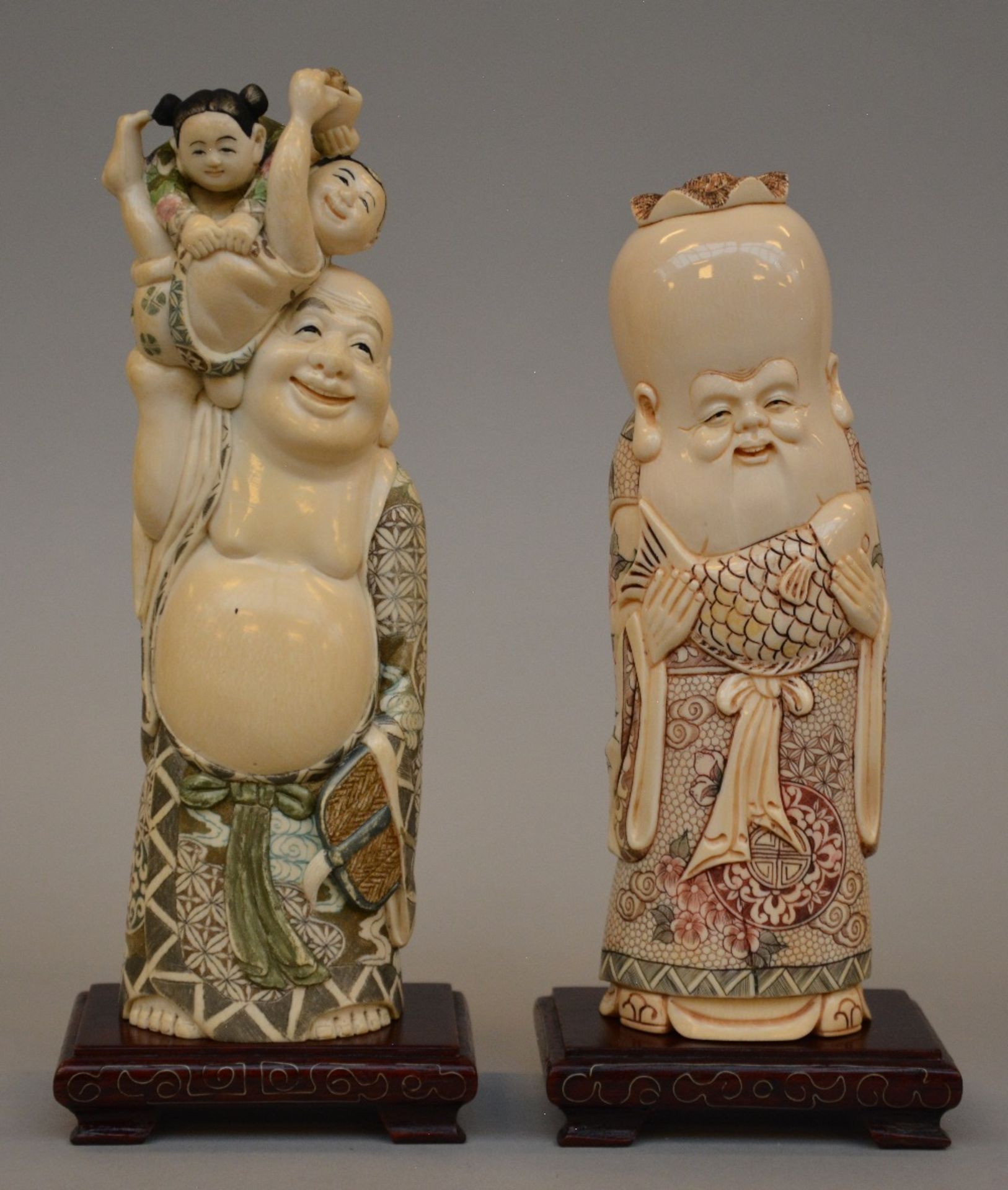 Two Japanese ivory figures on a wooden base depicting the laughing Hotei and Fukurokuju, scrimshaw