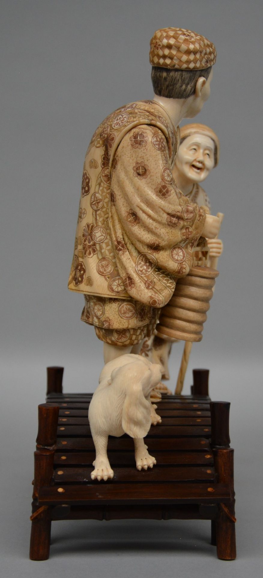 A charming Japanese ivory okimono depicting two figures and a dog on a bridge, red and black - Image 4 of 5