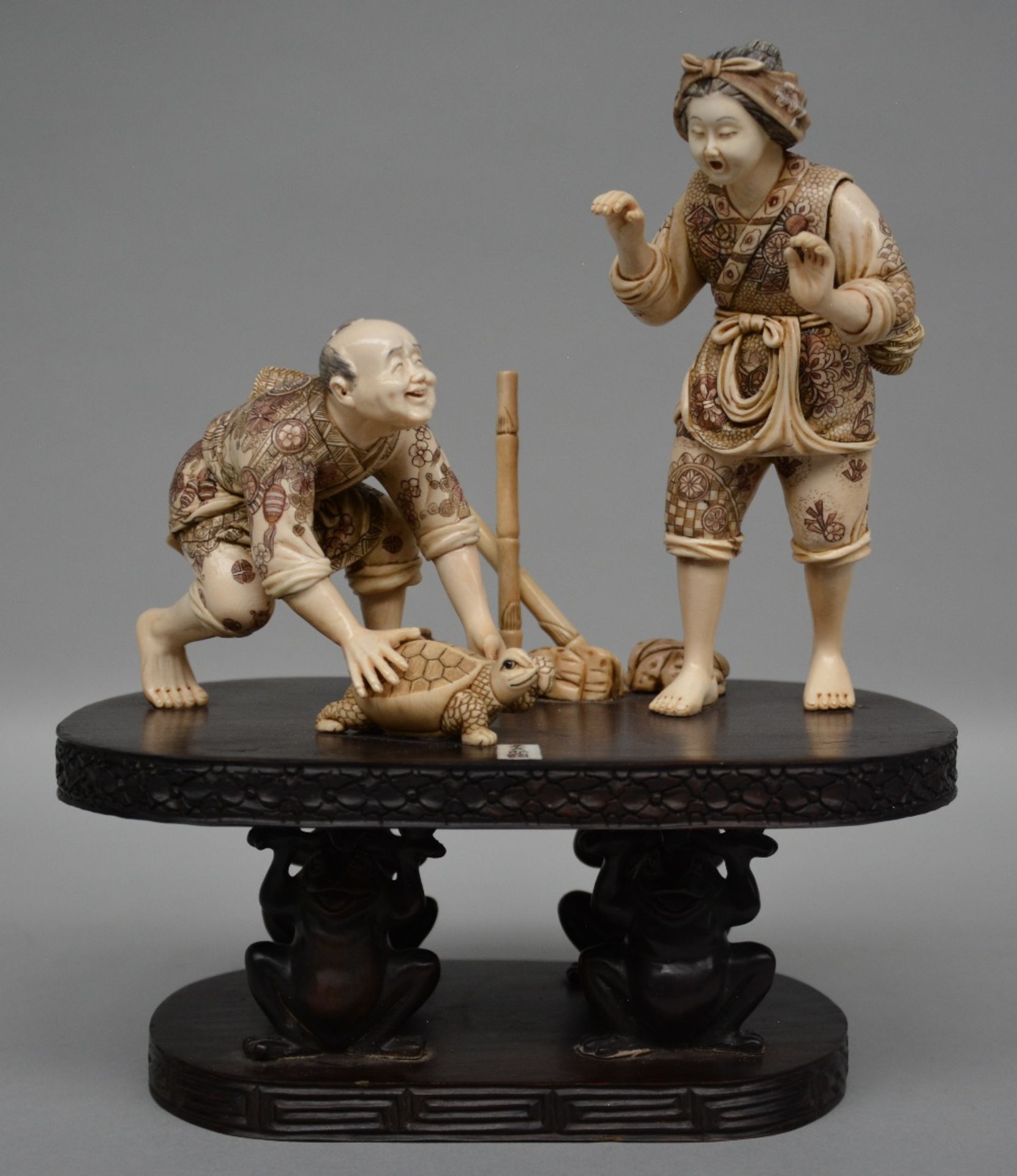 A charming Japanese ivory okimono of two figures playing with a tortoise, red and black scrimshaw