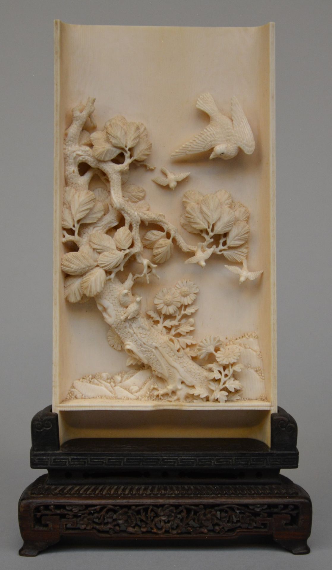 A Chinese ivory plaque carved in high relief, on a wooden base, early 20thC, H 23 cm (without base),