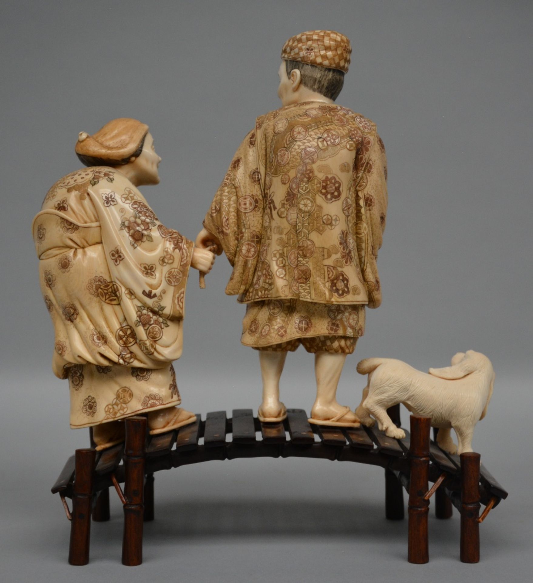 A charming Japanese ivory okimono depicting two figures and a dog on a bridge, red and black - Image 3 of 5