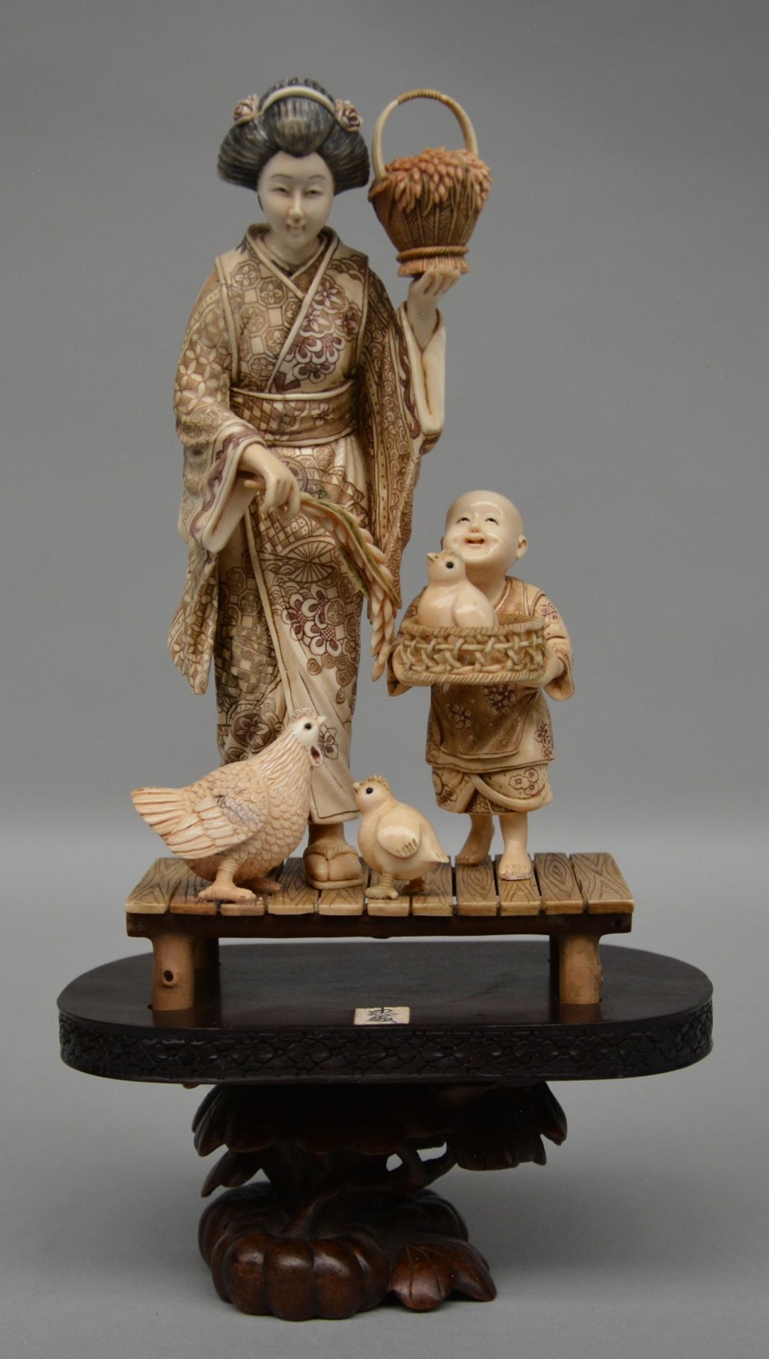 A charming Japanese ivory okimono decorated with red and black scrimshaw, on a wooden base, ca.