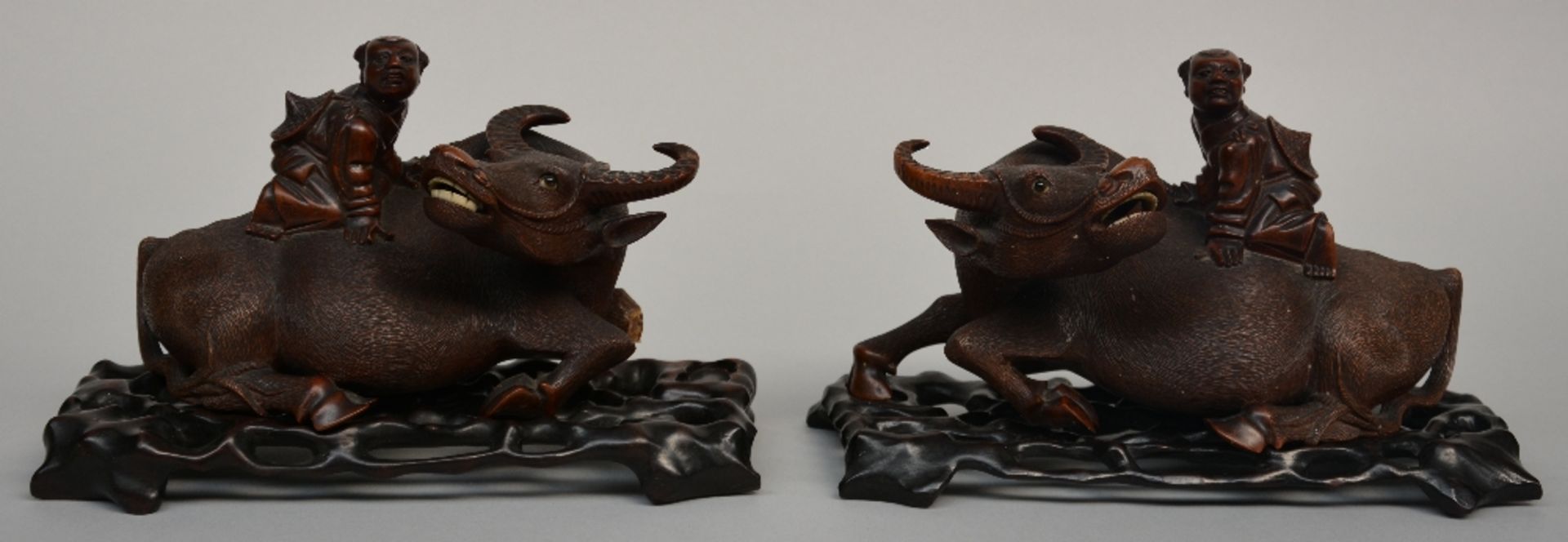 A pair of Chinese wooden carved children figures on a lying buffalo, on a wooden base, H 18 - B 29