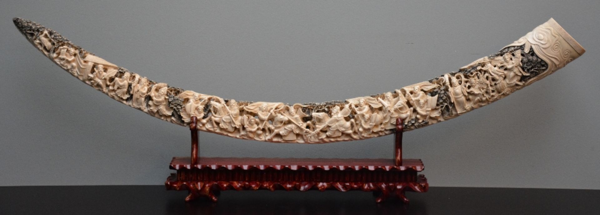 A Chinese carved ivory tusk on a wooden base, first half of 20thC, H 52 - W 158,5 cm