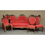 A 19thC richly carved rosewood drawing room set with red upholstering, comprising a settee and six