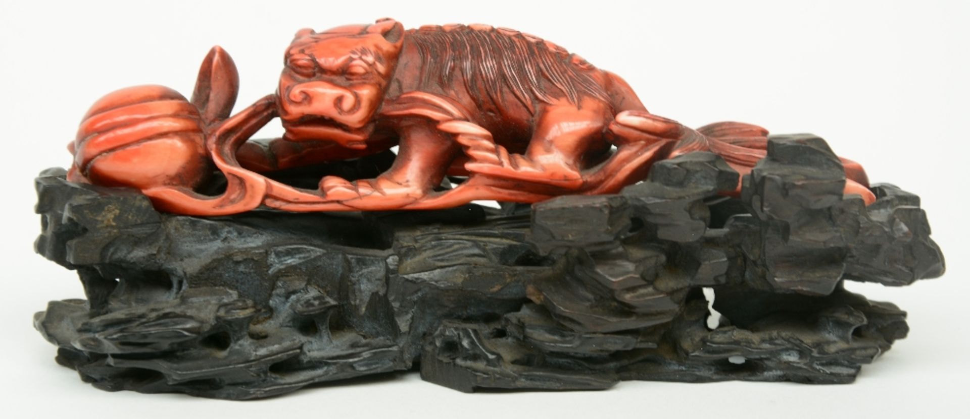 A Chinese monochrome red ivory sculpture depicting a mythological animal, on a wooden base, 19thC, H