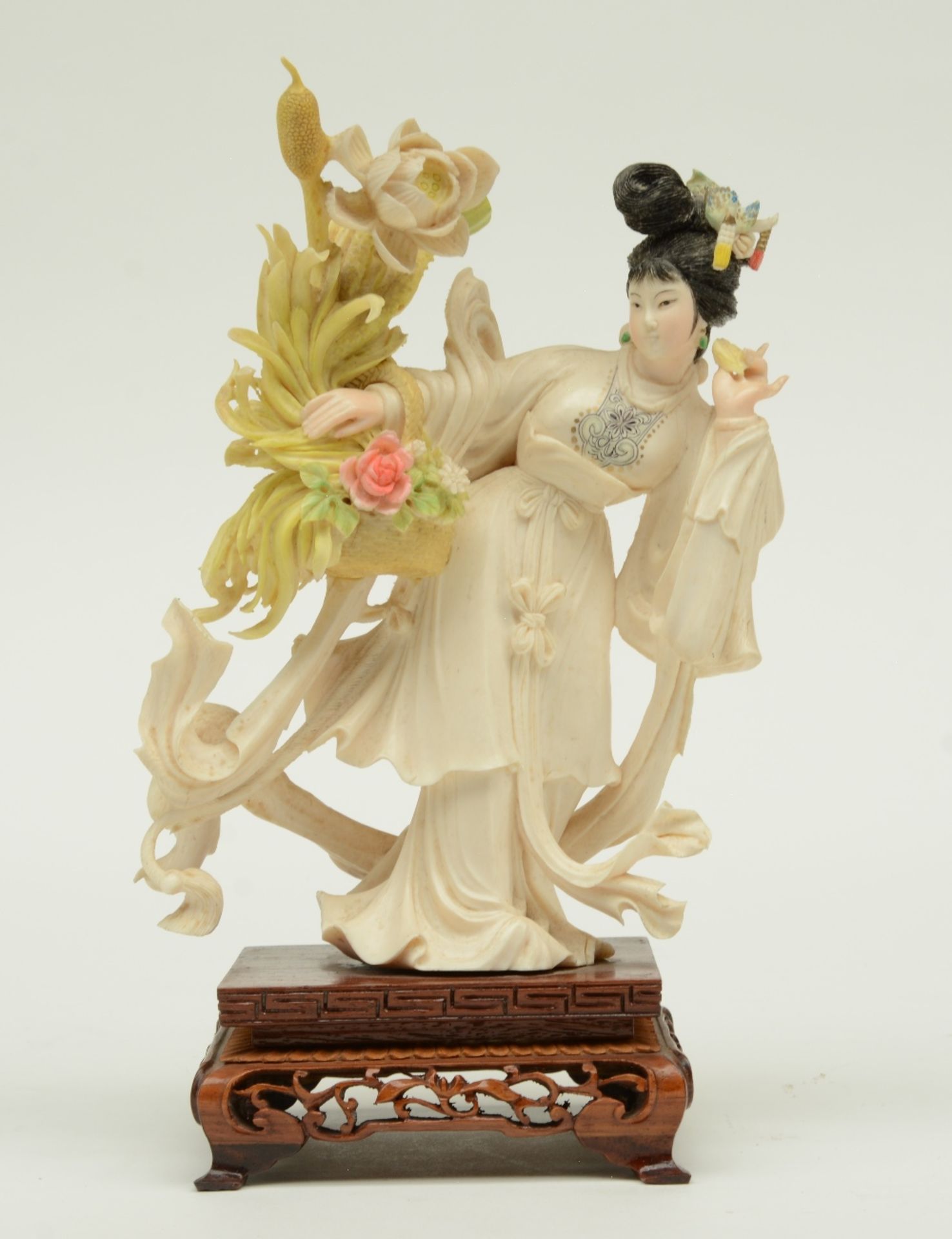 A Chinese ivory sculpture, polychrome decorated, depicting a court lady holding a flower basket,