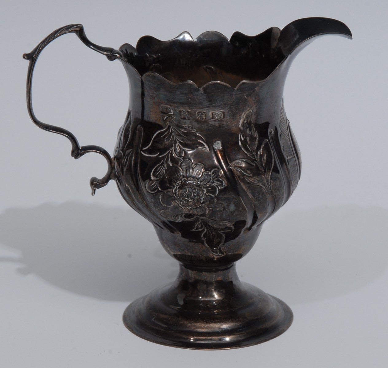 A George III Rococo silver baluster cream jug, embossed with a scrolling cartouche,