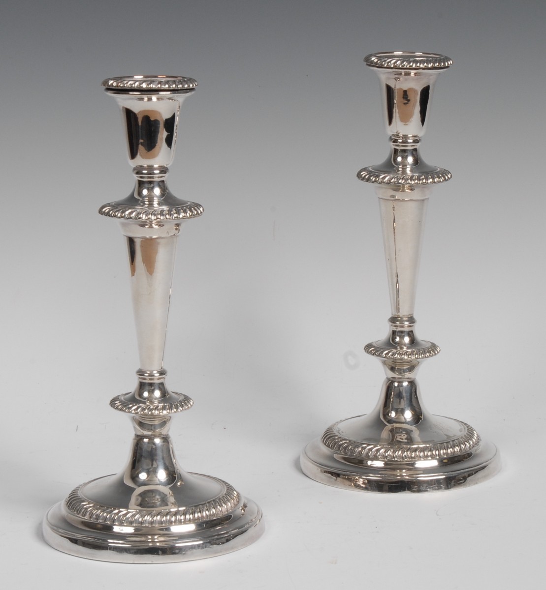 A pair of silver plated candlesticks, urnular nozzles, tapering cylindrical columns,