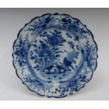 An 18th century Dutch Delft shaped circular plate, decorated with peonies, foliage and rockwork,