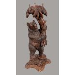 A 19th century Black Forest novelty torchere, carved as a young bear holding aloft a leafy branch,