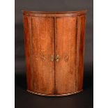 A George III oak bow fronted corner cupboard, the two doors with shell patera, 102cm high,