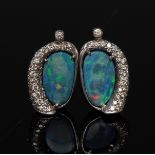 A pair of black opal and diamond earrings, each with an irregular oval black opal, flashing green,