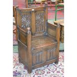 A monastic style hall settle, two carved panel back, hinged seat enclosing storage,