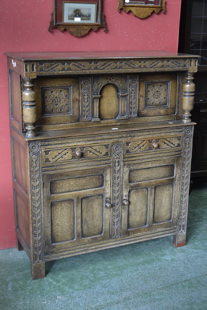 A monastic style court cupboard, blind fretworked frieze, two carved door cupboard to top,