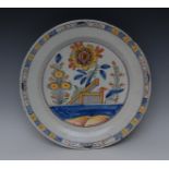 A Delft circular dish, painted in polychrome, with fence and stylised flowers,