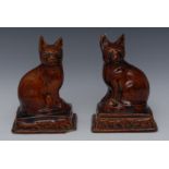 A pair of 19th century stoneware treacle-glaze mantel cats, seated to the left and right,