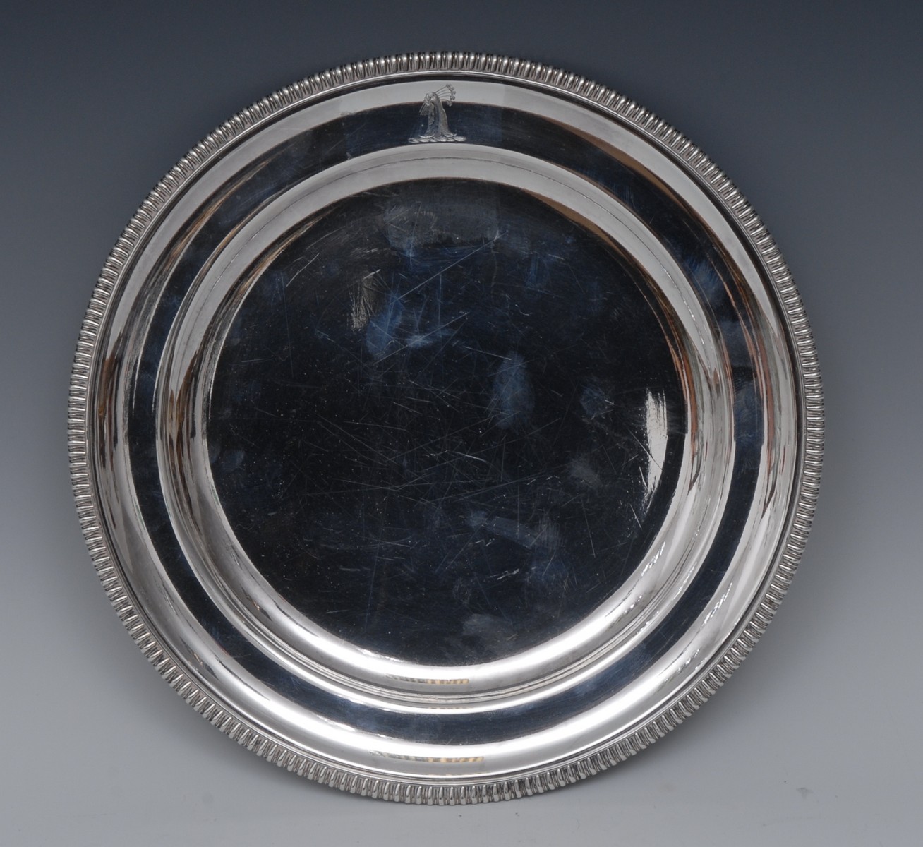 A silver plated circular under-plate, gadrooned rim, crested, 25cm diam,