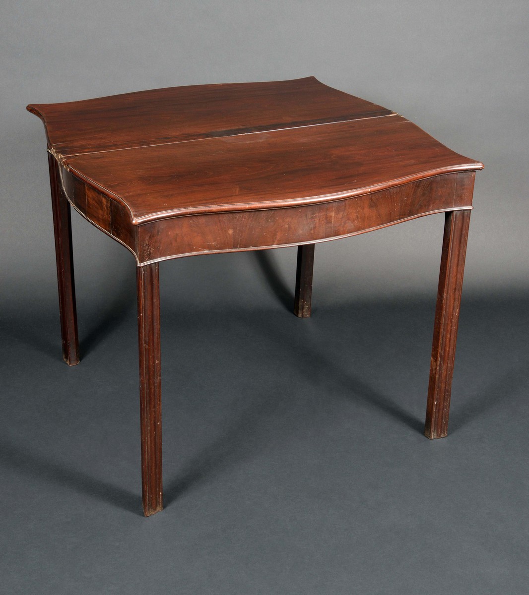 A George III mahogany serpentine tea table, folding top above a deep frieze, moulded legs,