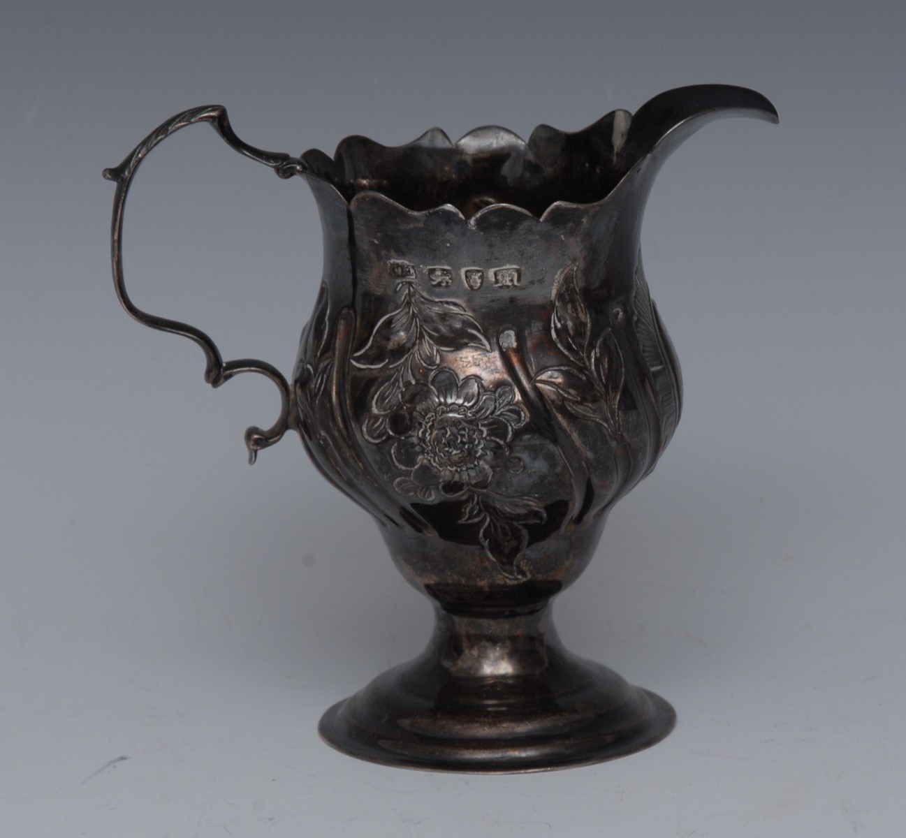 A George III Rococo silver baluster cream jug, embossed with a scrolling cartouche,